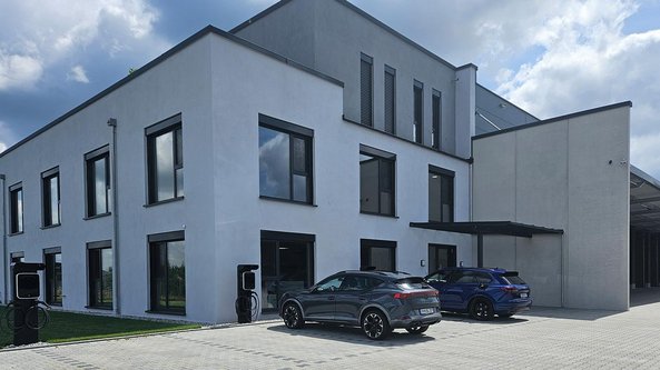 Ein modernes, zweigeschossiges Gebäude mit großen Fenstern und einem klaren, minimalistischen Design, umgeben von grünem Rasen.